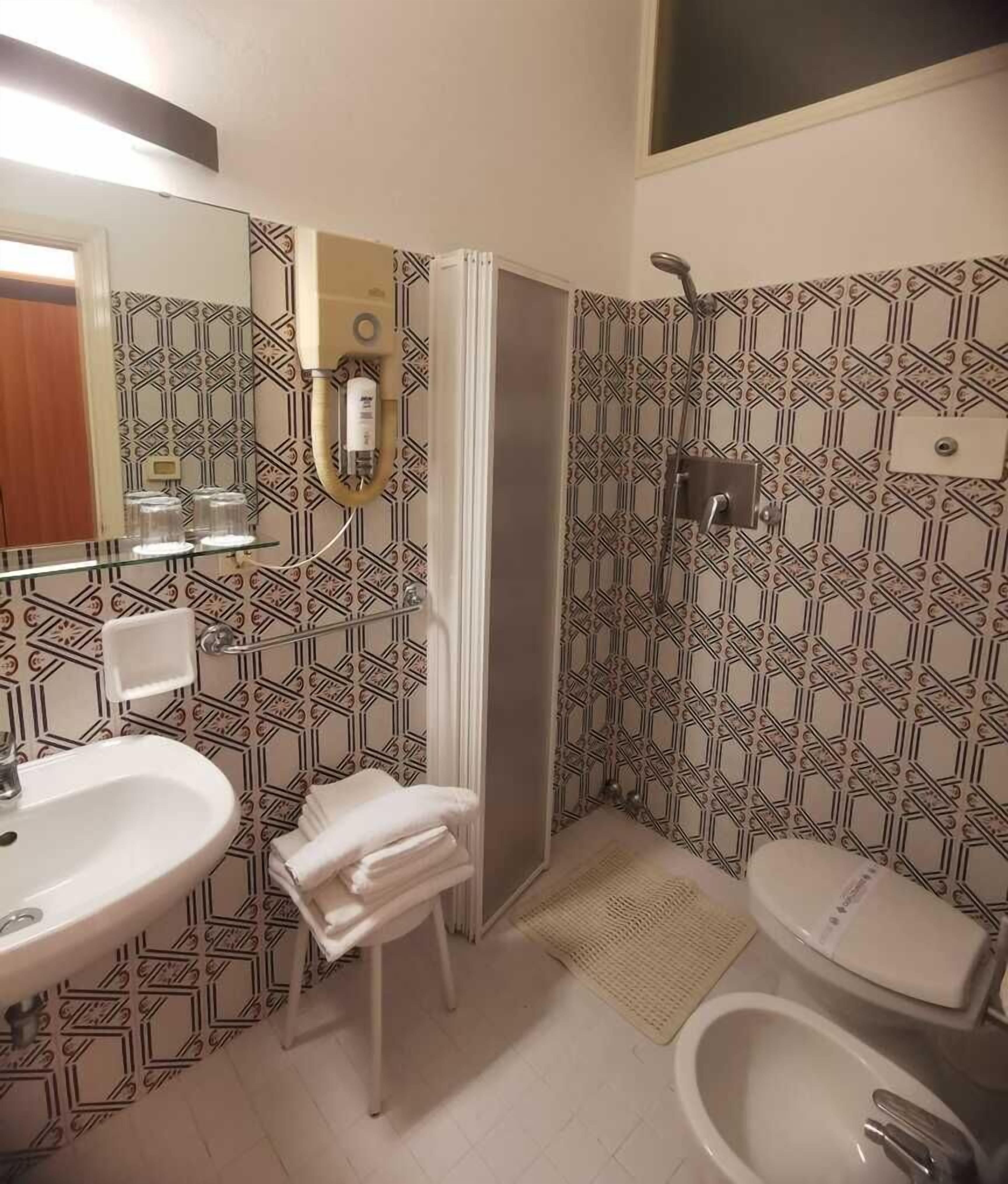 Un baño con salpicadero de azulejos estampados, un lavamanos blanco, un inodoro y una zona de ducha.