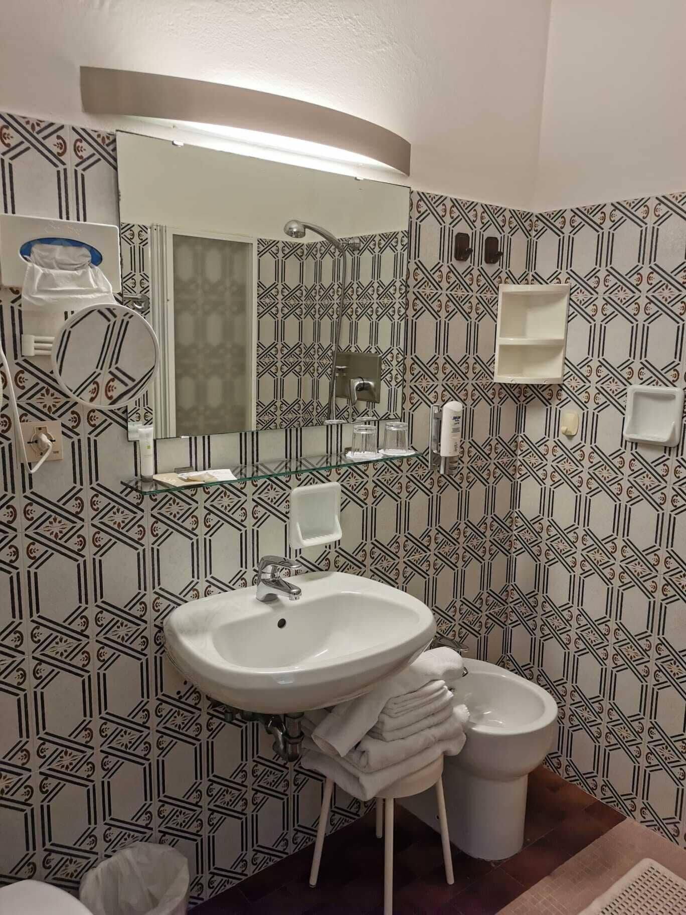 A bathroom with a white sink, mirror, and toilet. The walls have a geometric patterned tile design.