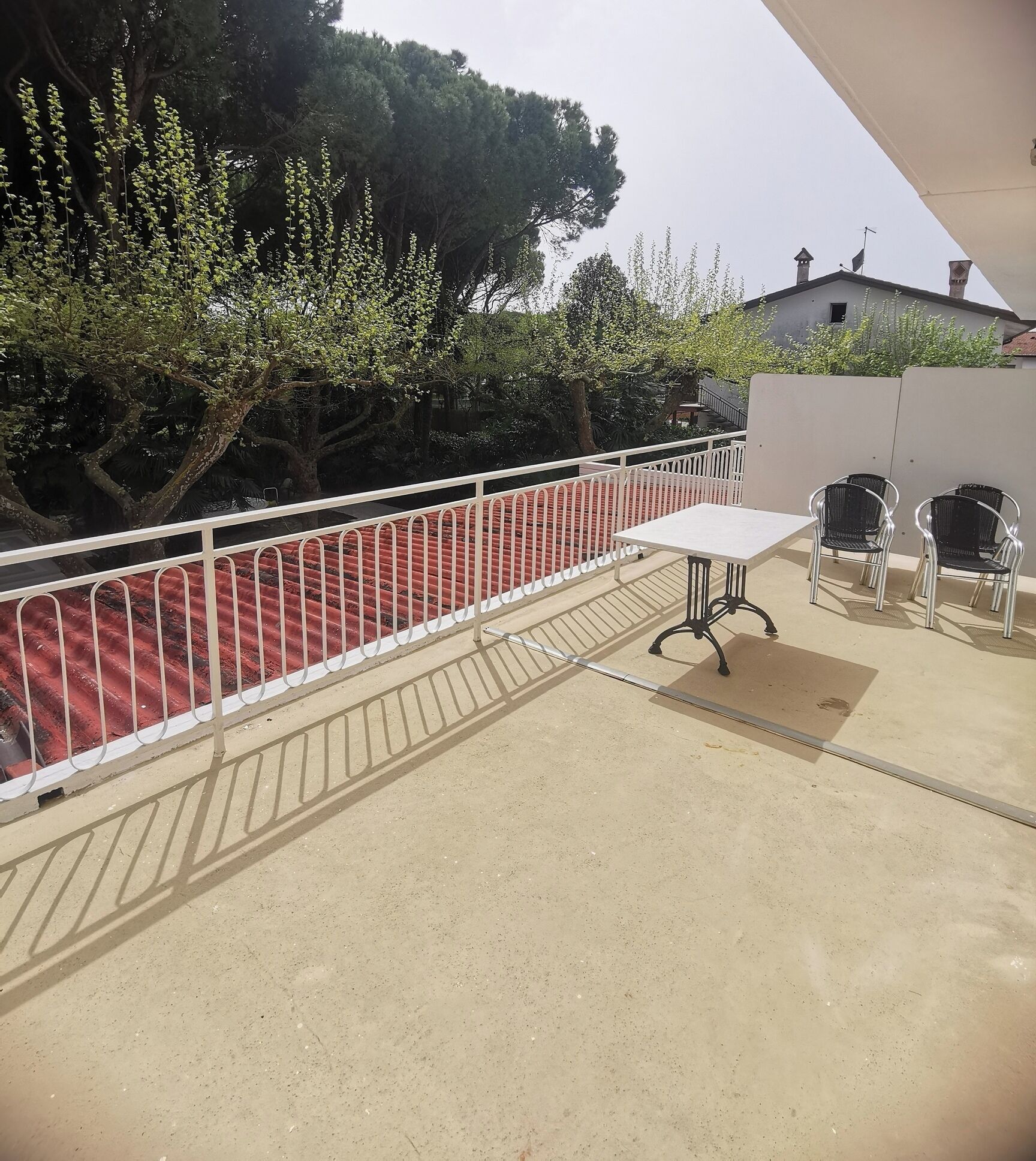 A balcony with a white table and four chairs, a red railing, and trees in the background.