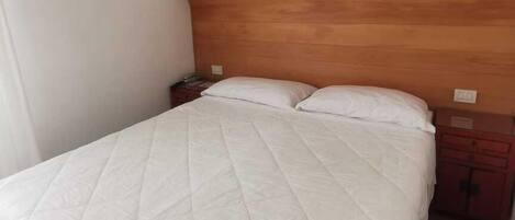 A single bed with a wooden headboard, white bedding, and a nightstand with a lamp.