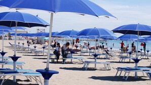 A beach with rows of blue umbrellas and white lounge chairs. - Hotel Valdor (Cavallino-Treporti)