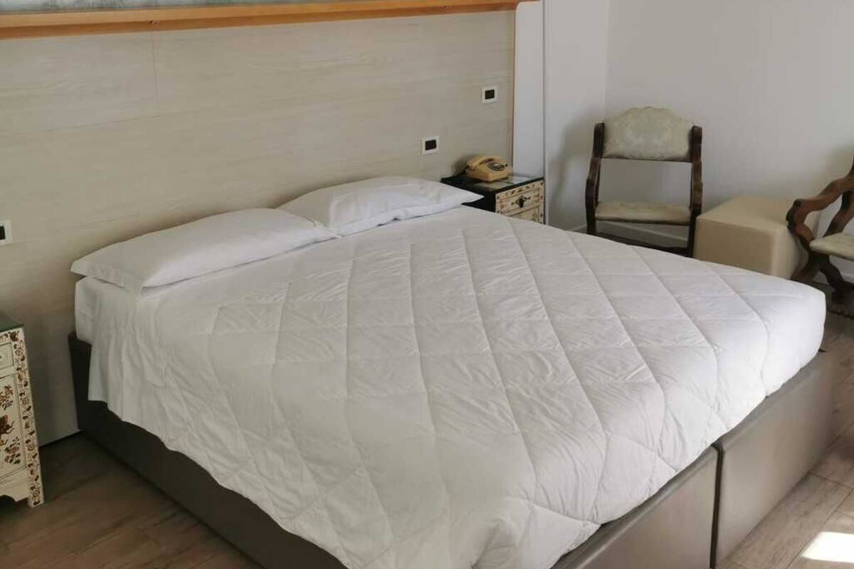 A bedroom with a large bed, a wooden headboard, a nightstand with a telephone, a chair, and a painting on the wall.