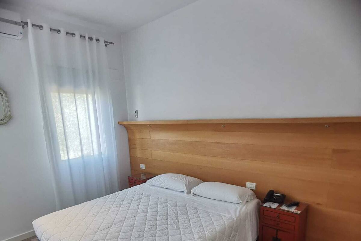 A bedroom with a bed, wooden headboard, bedside table, and a nightstand.