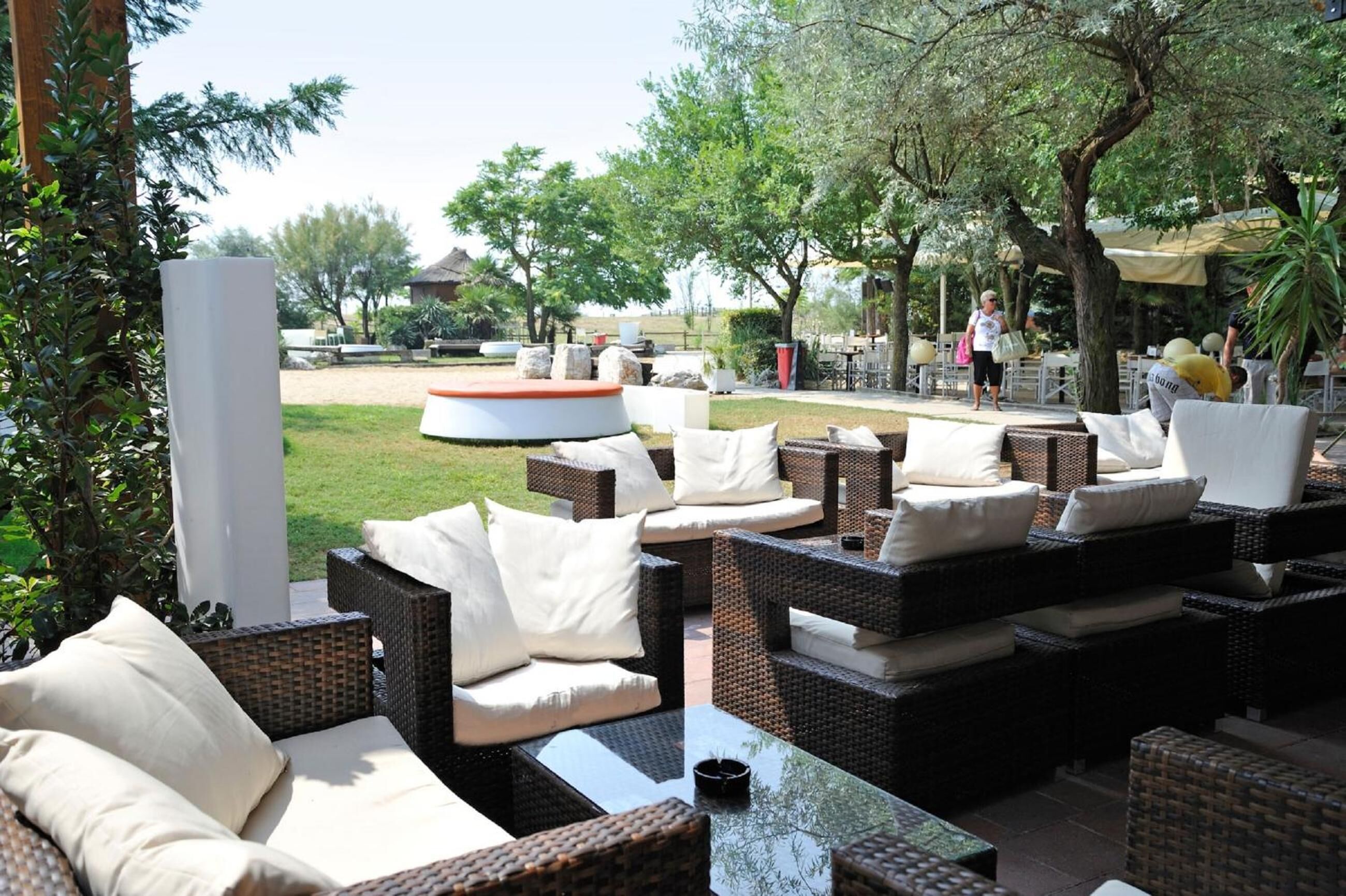 An outdoor seating area with wicker furniture and white cushions, surrounded by greenery and trees.