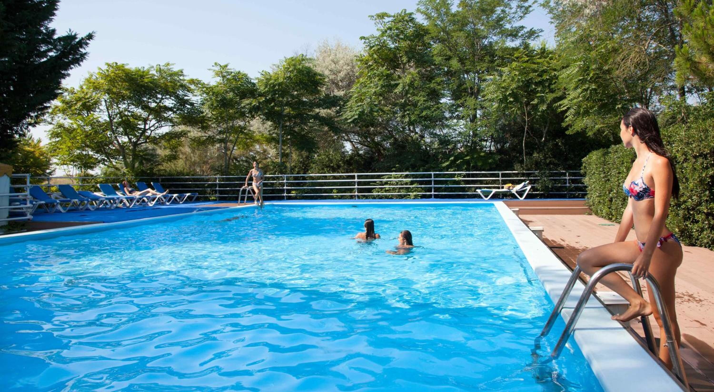 A swimming pool with clear blue water, surrounded by lounge chairs and a metal railing.