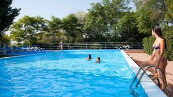 A swimming pool with clear blue water, surrounded by lounge chairs and a metal railing.