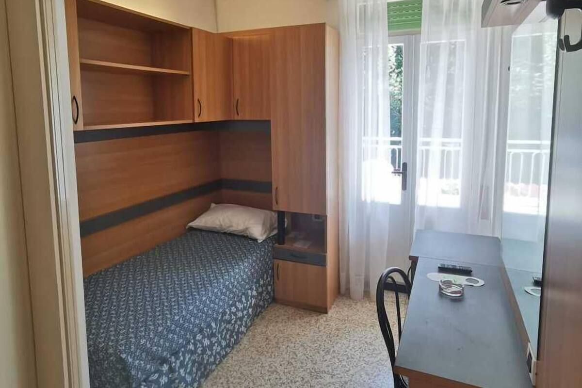 A compact room with a bed, a desk, and a ceiling fan.