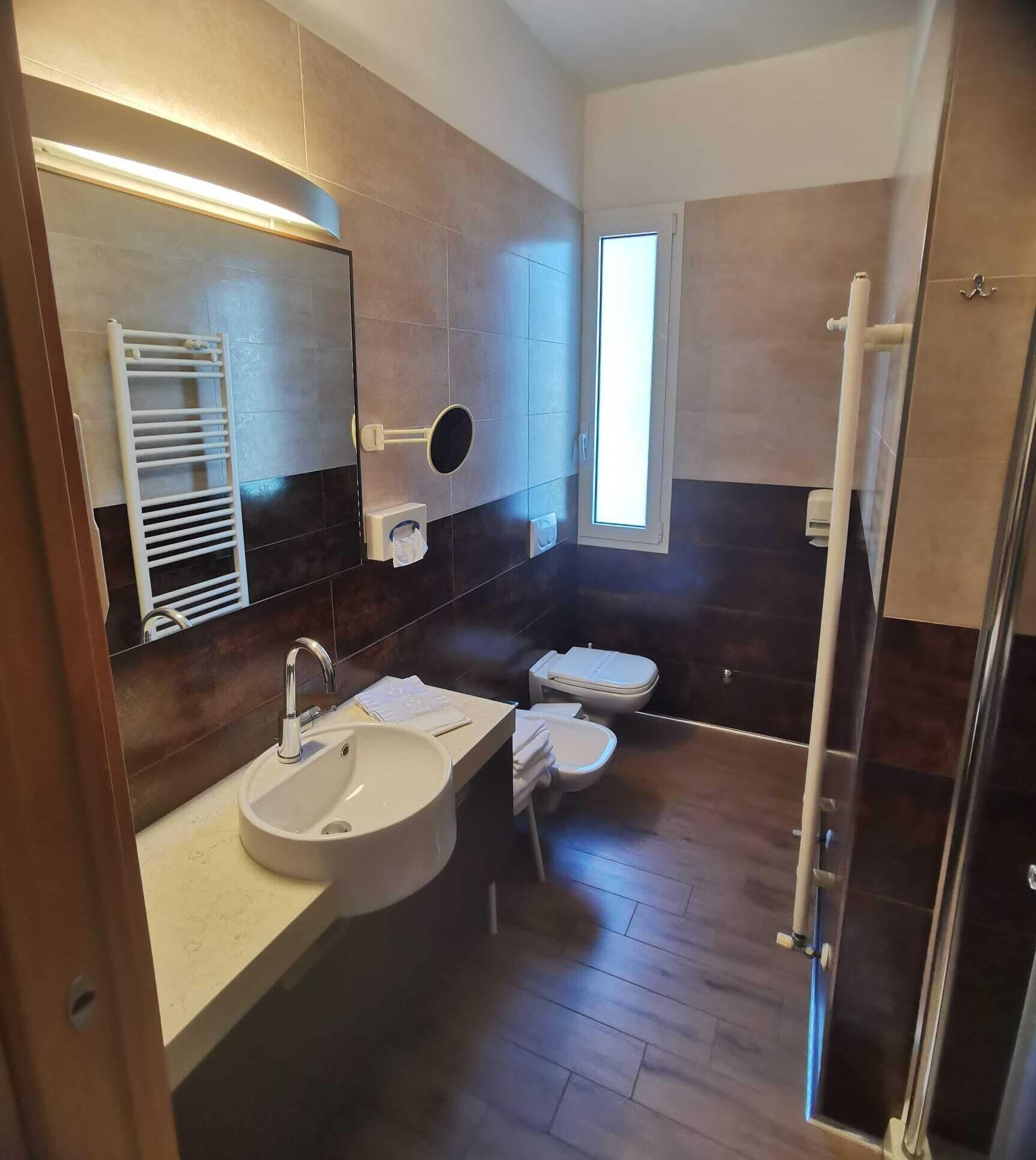 Un baño moderno con un espejo grande, un lavamanos, un inodoro y una zona de ducha.