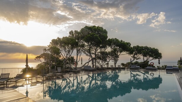 Zona de piscina con sillones de descanso y vista al mar al atardecer.