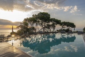A poolside area with lounge chairs and a view of the sea at sunset. - Parador de Aiguablava (Begur)