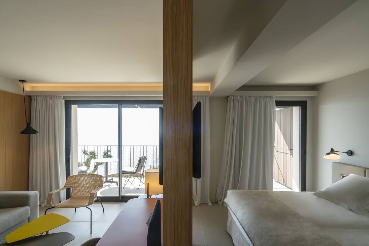 Ein Hotelzimmer mit Bett, einer Sitzecke, einem Sessel, einem kleinen Tisch und einem Balkon mit Blick.