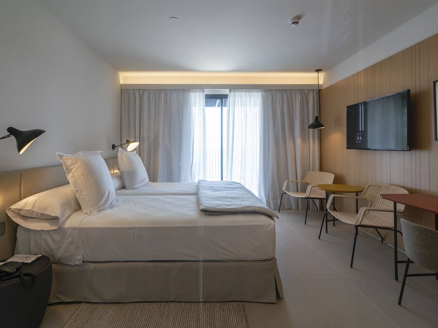 Habitación de hotel con cama, dos lámparas de noche, televisor, mesita y una silla.