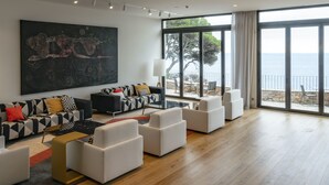 Una sala de estar moderna con un cuadro abstracto grande, un juego de sofá y vista al mar a través de ventanas amplias.