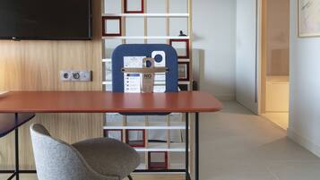 A modern room with a wooden wall, a flat-screen TV mounted above a wooden desk, a blue chair, and a white shelving unit with red accents.