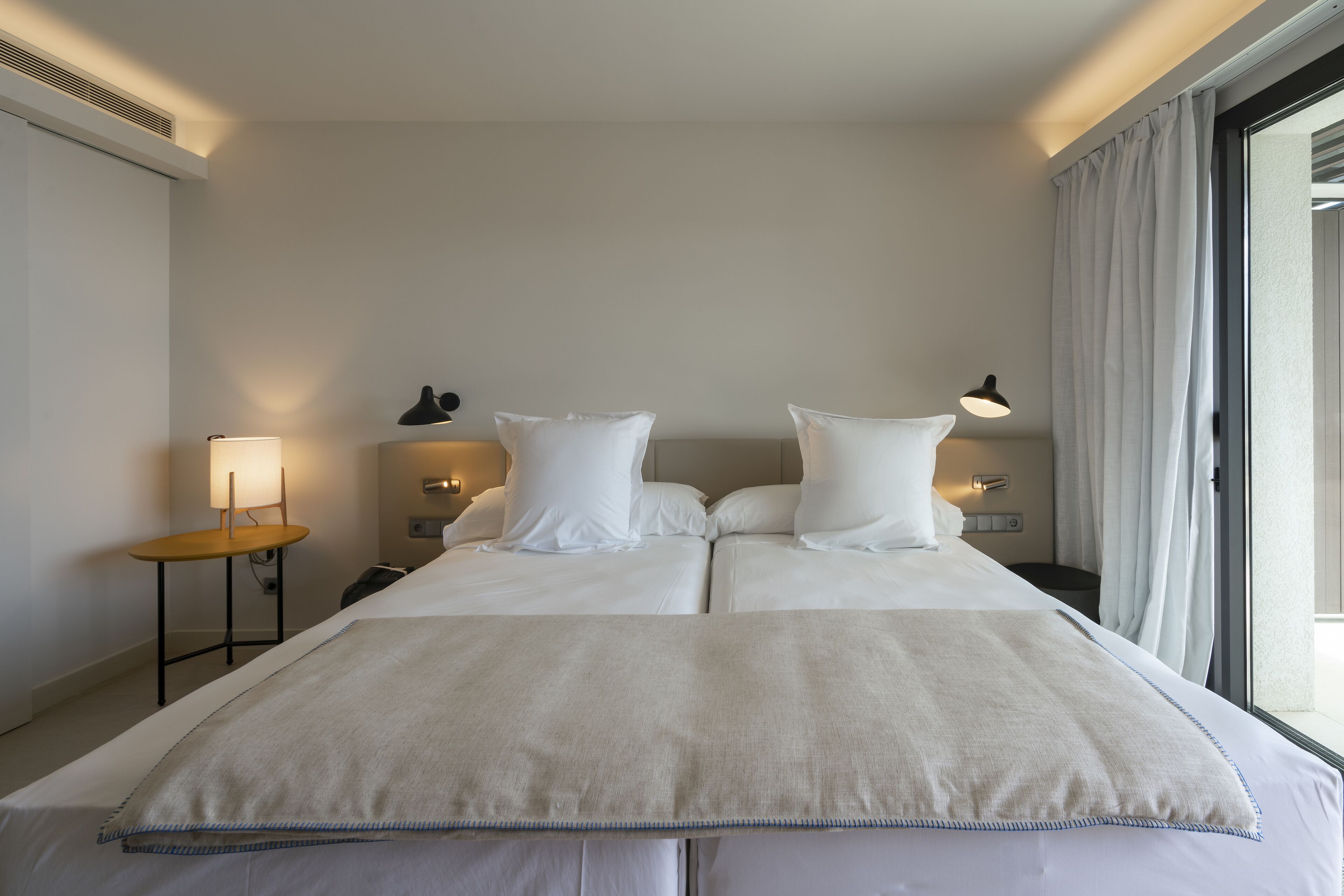 A hotel room with a large bed, two bedside tables, a lamp, and a window with curtains.