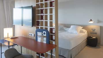 Habitación de hotel con cama, escritorio y silla, televisor y una partición de madera con estantes.
