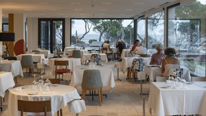 Un restaurante con mesas dispuestas para comer, amplias ventanas que ofrecen vistas al mar y una decoración de interiores moderna.