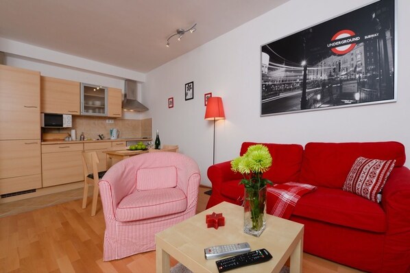 A compact living space with a kitchenette, a red sofa, a striped chair, and a table with a vase and remote controls. - Aboriginal Budapest Apartments (Budapest)