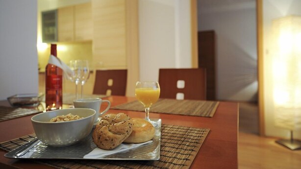 Un desayuno con un tazón de cereal, dos croissants, un vaso de jugo de naranja y una botella de agua sobre una mesa.