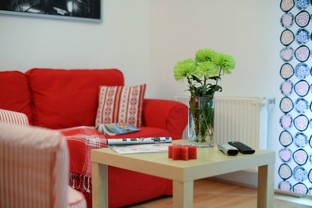 Ein Wohnzimmer mit einem roten Sofa, einem kleinen Tisch mit Blumenvase und einer Wand mit kreisförmigen Mustern.