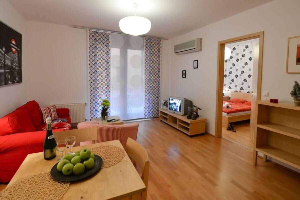 Ein modernes Wohnzimmer mit einem roten Sofa, einem Holzespeisetisch mit einer Flasche und Gläsern sowie einem Fernseher auf einem Holzboden.