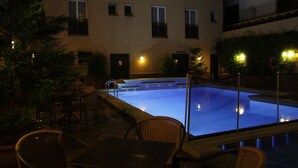 Una piscina con area relax a livello, circondata da sedie e tavoli, con un edificio sullo sfondo.