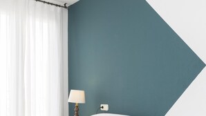 Una camera da letto con un letto, tende bianche, un comodino con una lampada e una parete verde acqua.