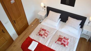A neatly made bed with a red and white blanket, two bedside tables with lamps, a wooden door, and a wall-mounted deer head decoration.