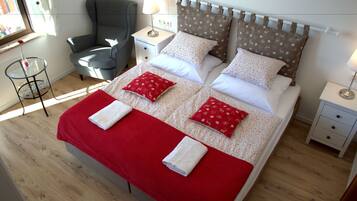 A neatly made bed with a red blanket and pillows, a grey armchair, and a small table with a lamp.