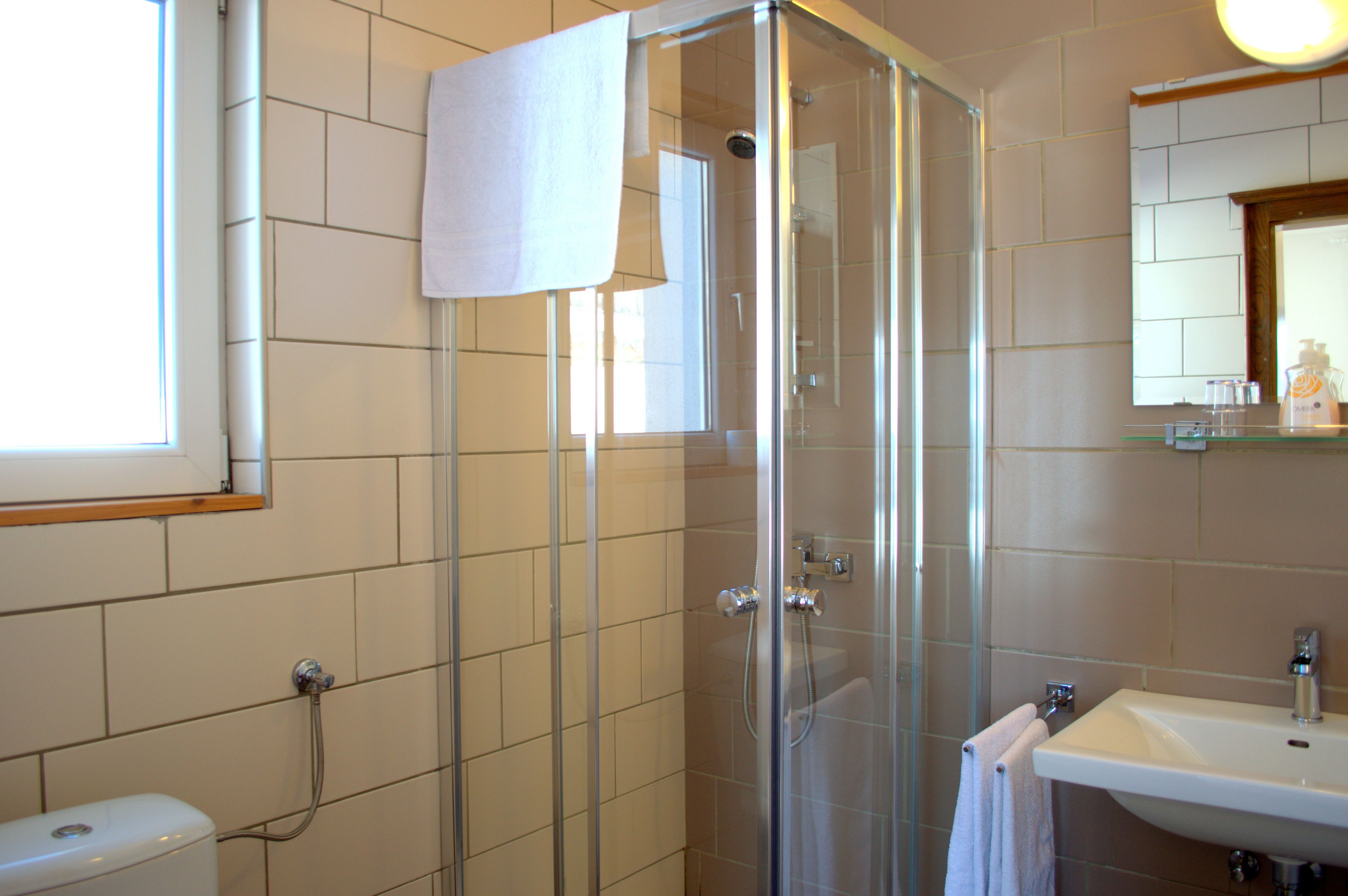 Un baño moderno con ducha envuelta en vidrio, inodoro y lavamanos con espejo superior.
