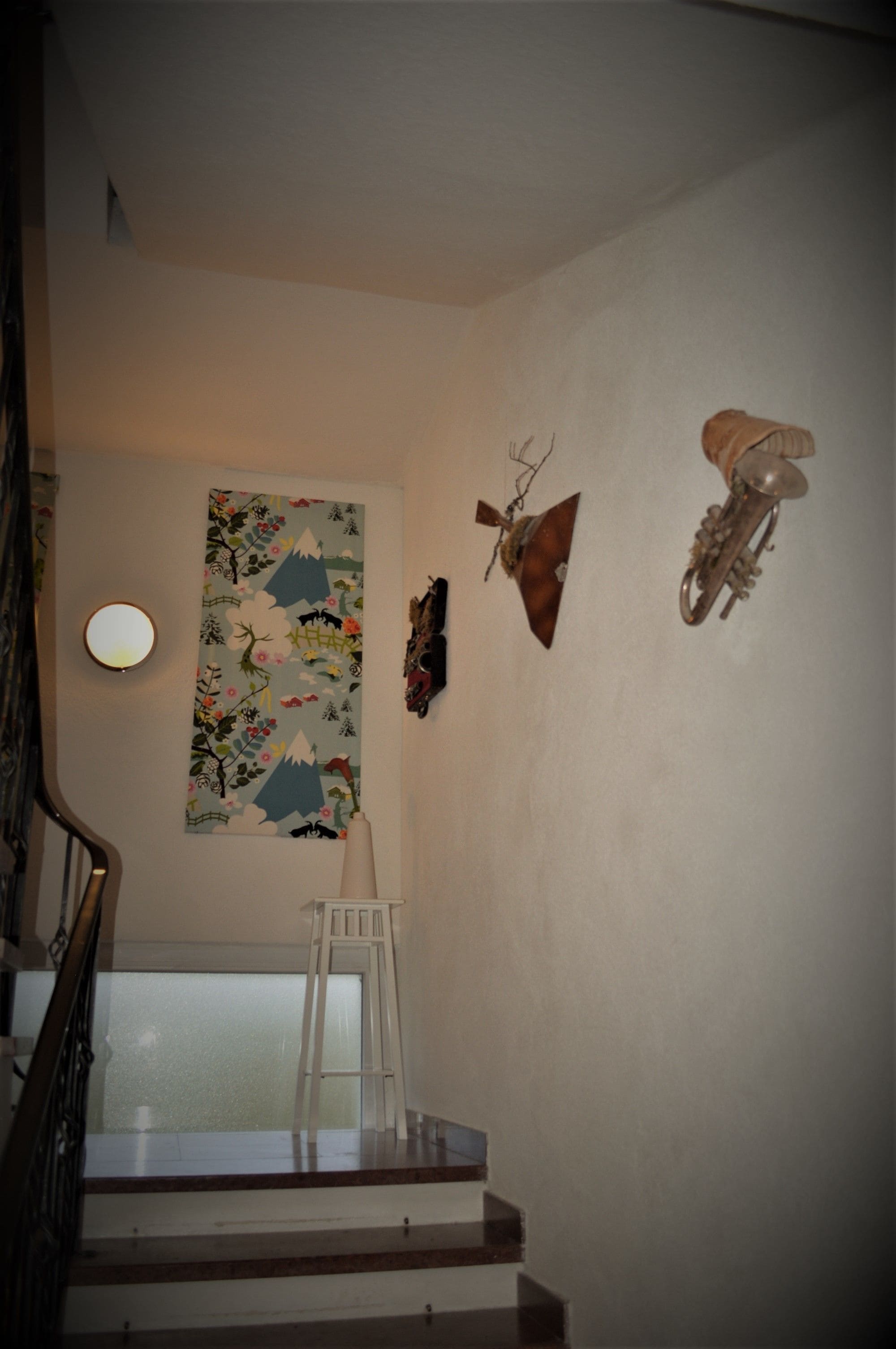 Una escalera con una silla blanca, un muro decorado con un tapiz floral y una cabeza de animal montada.