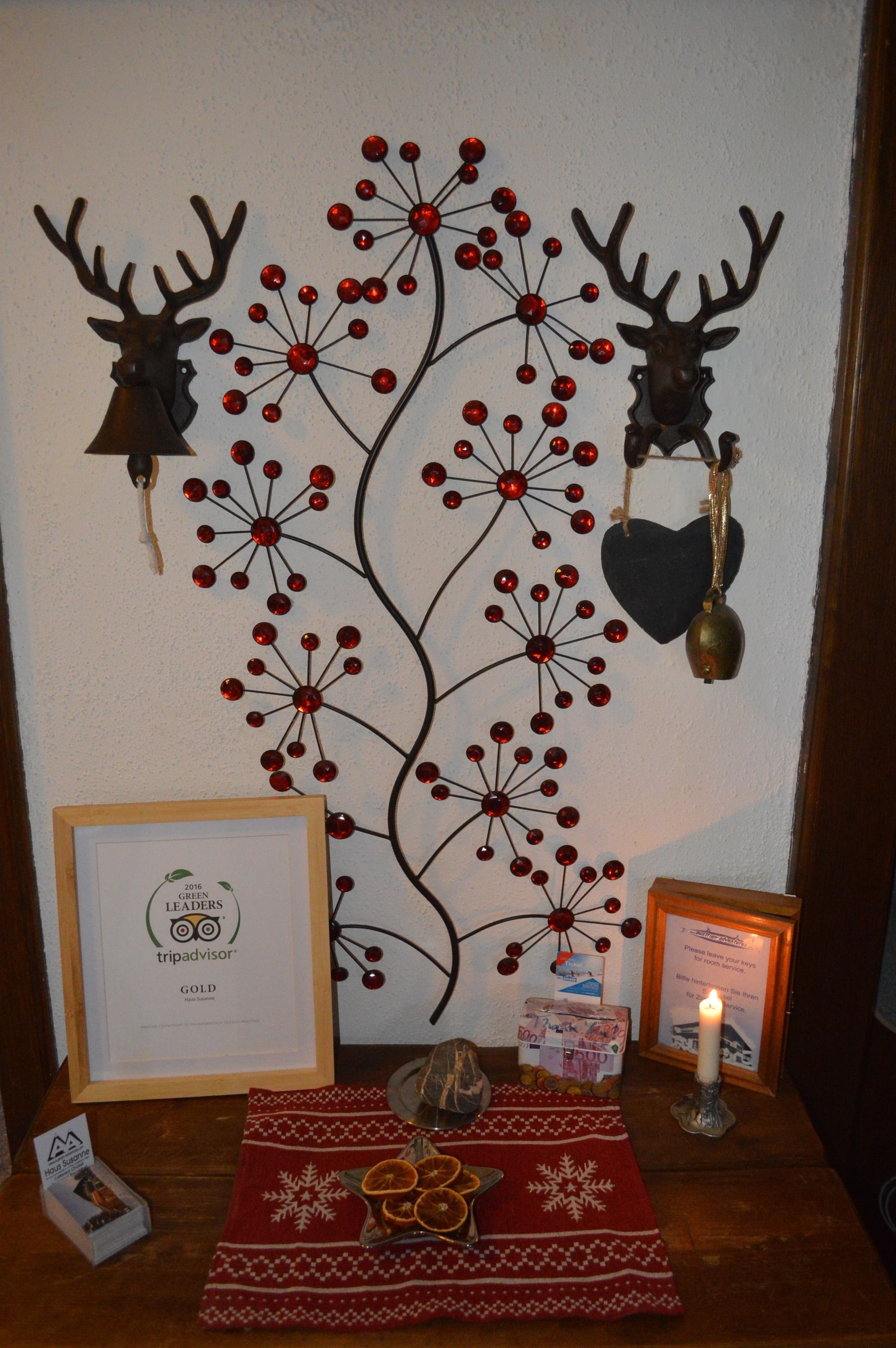 Wanddecoratie met rode bessen, hertenkoppen, een ingelijst certificaat, een kaars en een tafel met een rode doek en gedroogde sinaasappelschijfjes.
