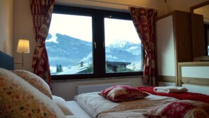 A bedroom with a large window, a bed with floral bedding, a red throw blanket, and a wooden headboard. - Haus Susanne (Radstadt)