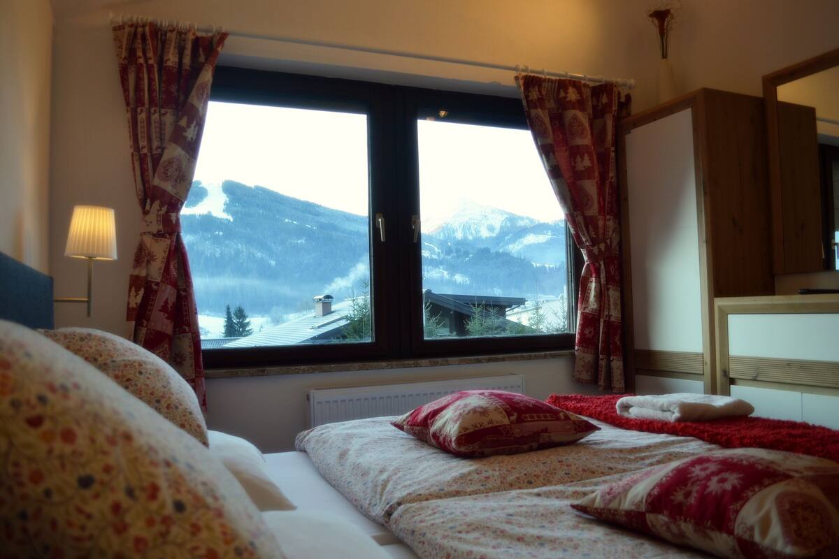 A bedroom with a large window, a bed with floral bedding, a red throw blanket, and a wooden headboard.