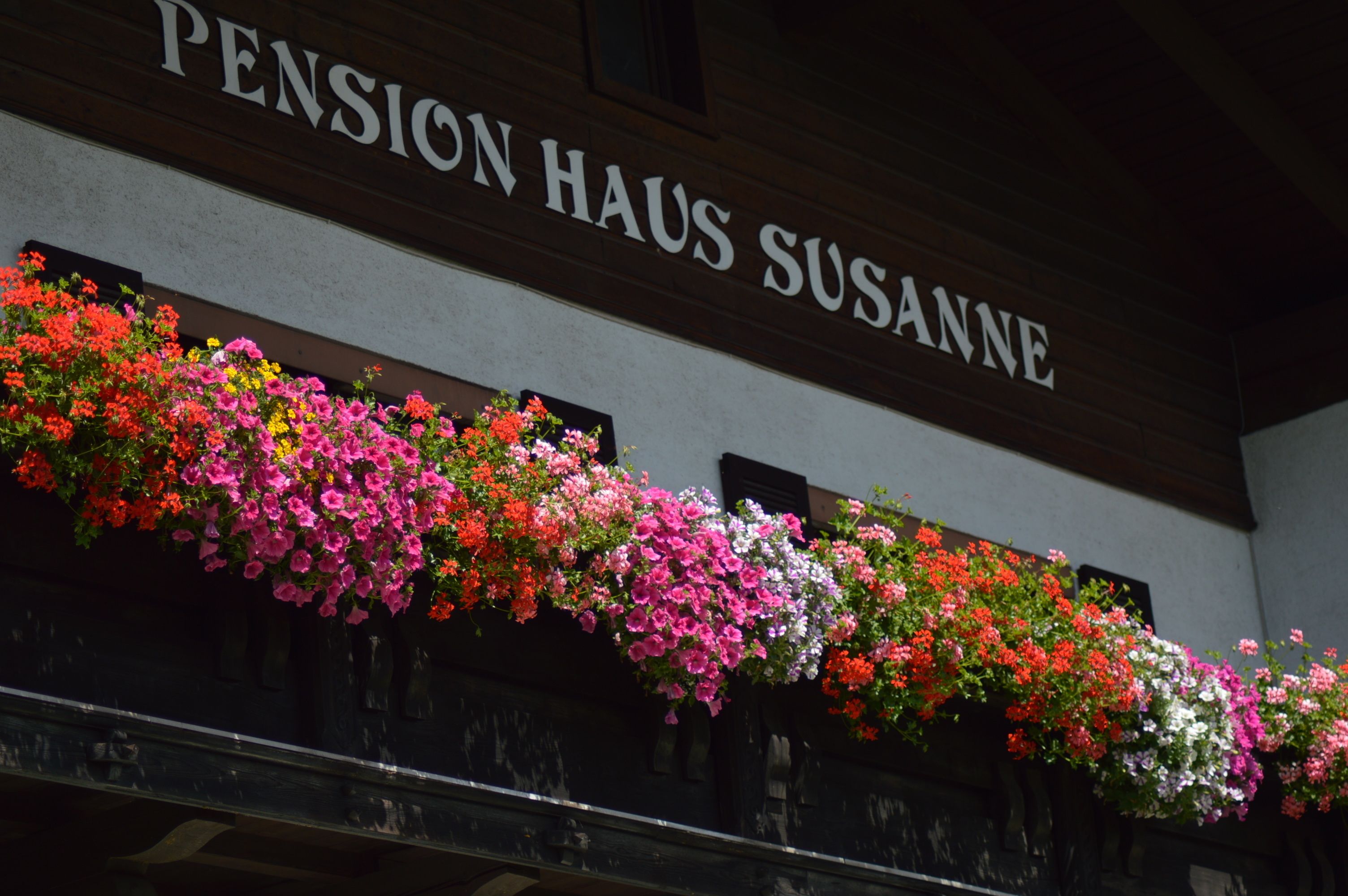 A building with a sign reading "Pension Haus Susanne" and a balcony with colorful flower boxes.