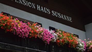 A building with a sign reading "Pension Haus Susanne" and a balcony with colorful flower boxes.