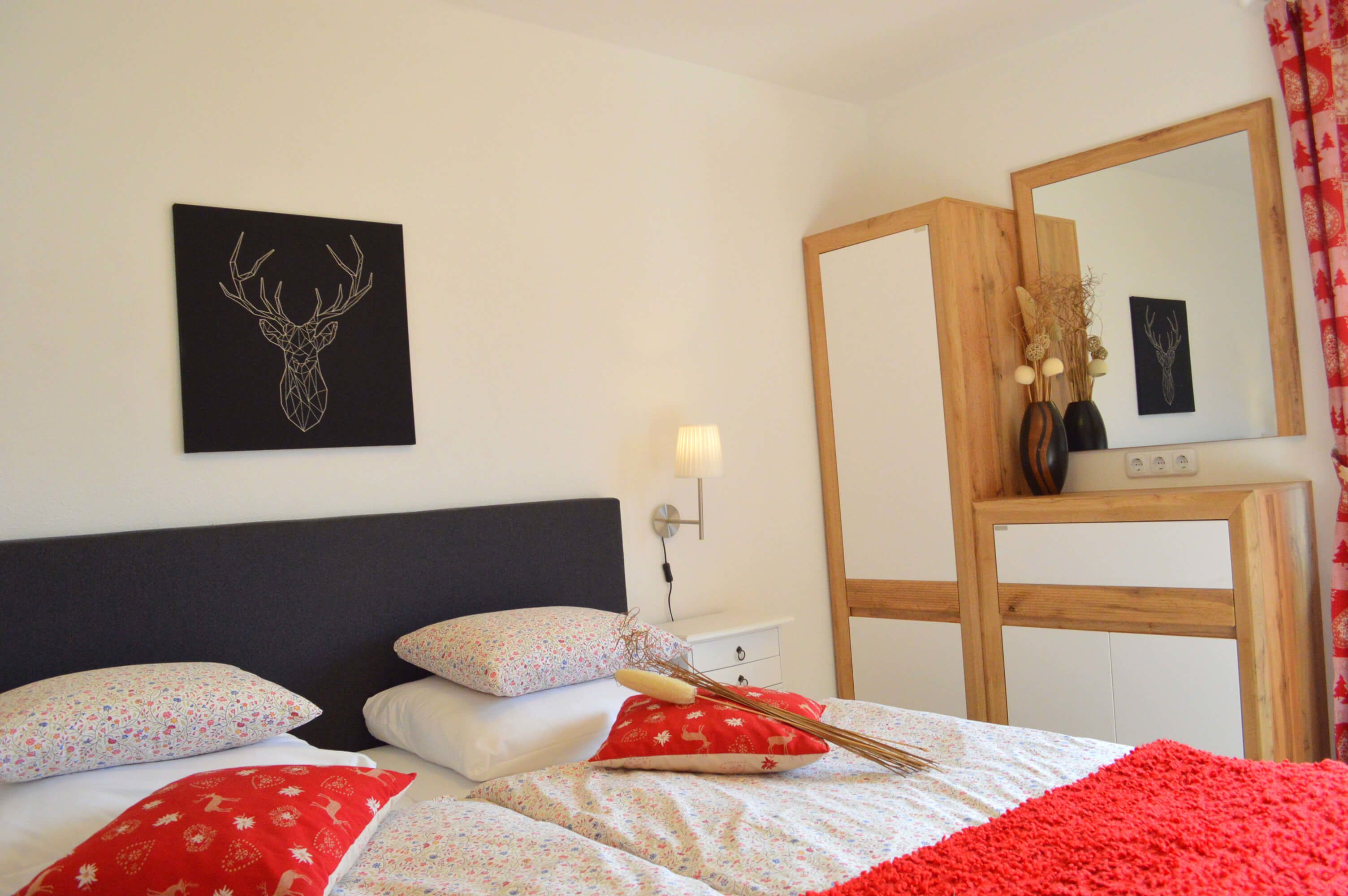 Een keurig opgemaakt slaapkamer met een bed, kussens, een nachtkastje, een spiegel en decoratie aan de muur.