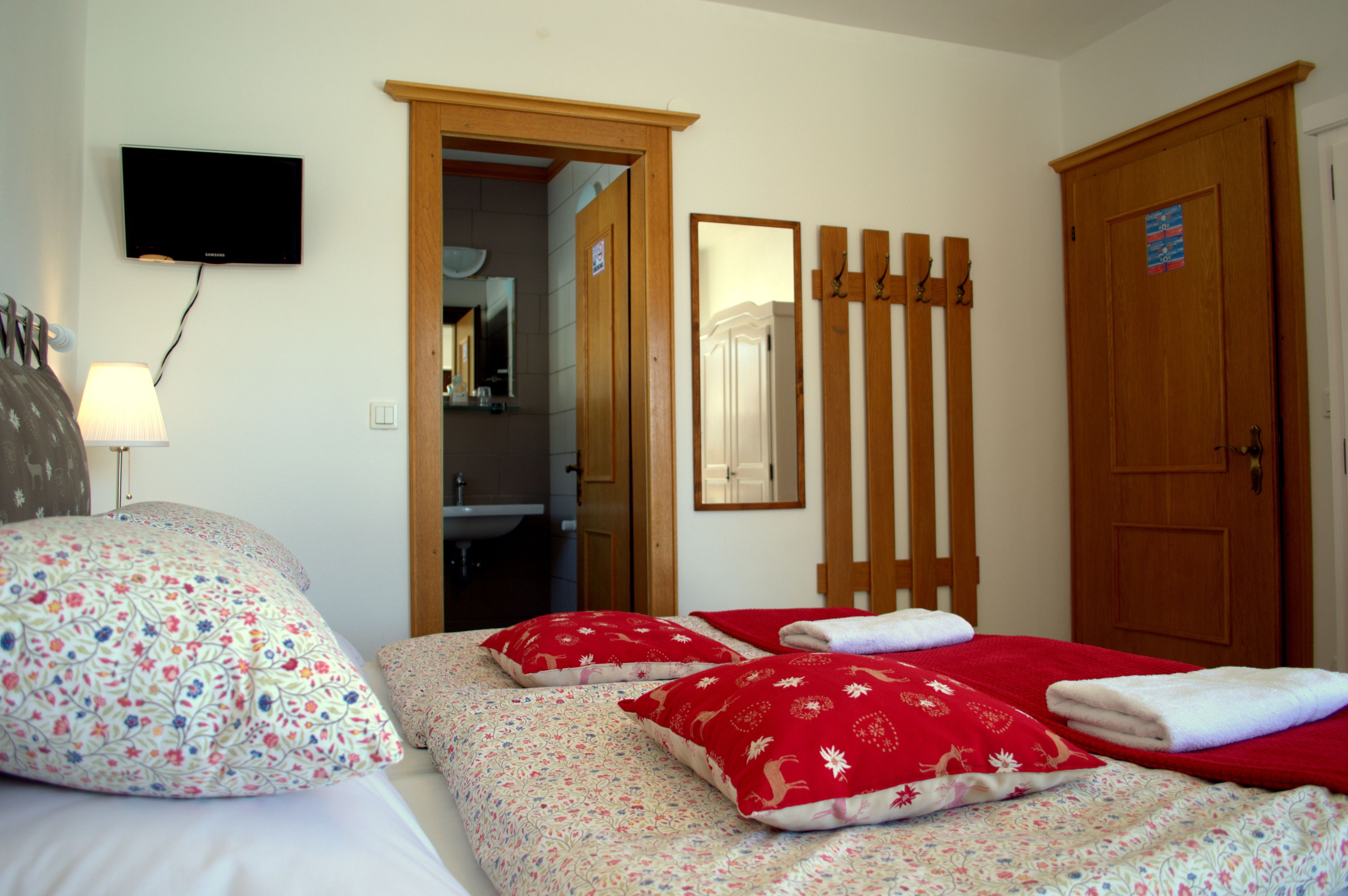 A hotel room with a bed, a TV mounted on the wall, a wooden door, and a mirror.