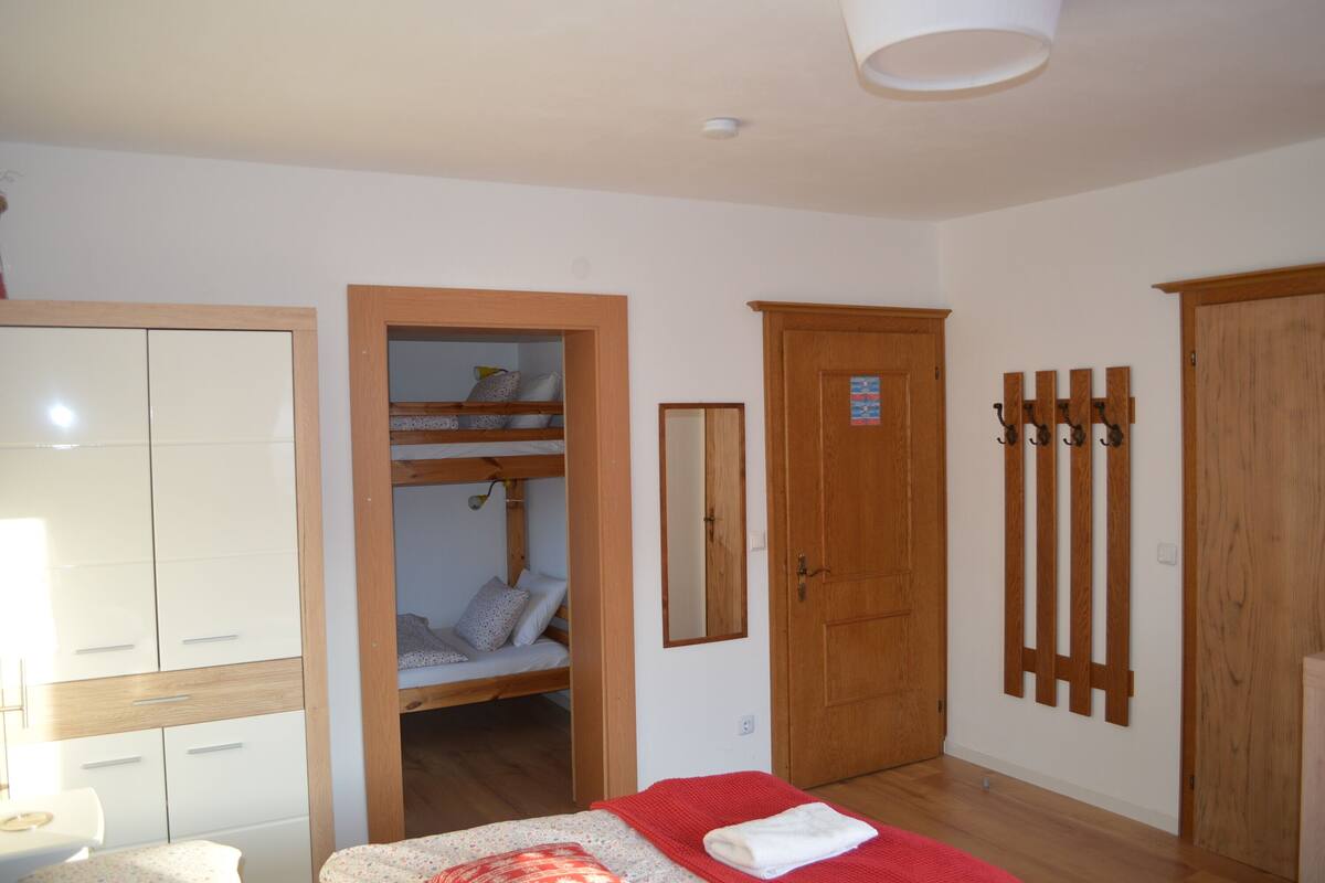 A bedroom with a bunk bed, a wardrobe, a mirror, and a door with a coat rack.