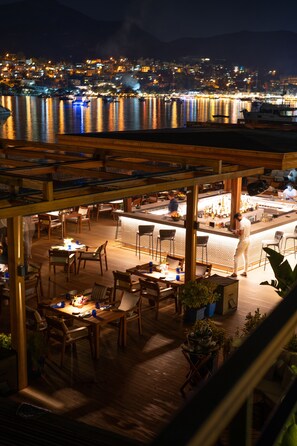 An outdoor dining area with wooden tables and chairs, a bar, and potted plants. - No 81 Hotel (Bodrum)