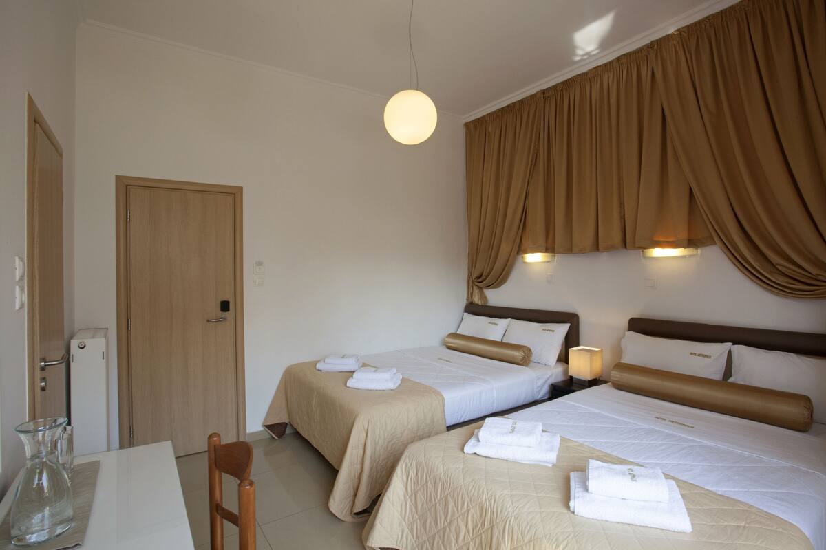 A hotel room with two beds, a dining table, a refrigerator, and a hanging light fixture.