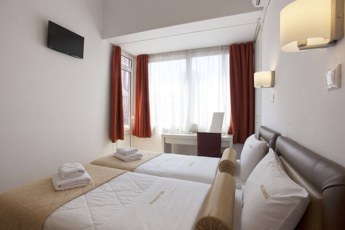 A hotel room with two beds, a desk, and a TV on the wall.