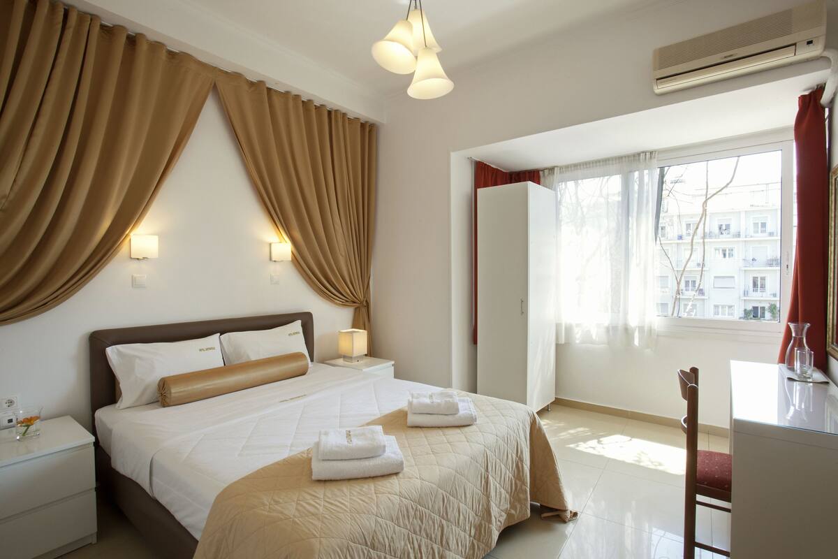 A hotel room with a large bed, bedside lamps, a desk with a chair, and a window with curtains.