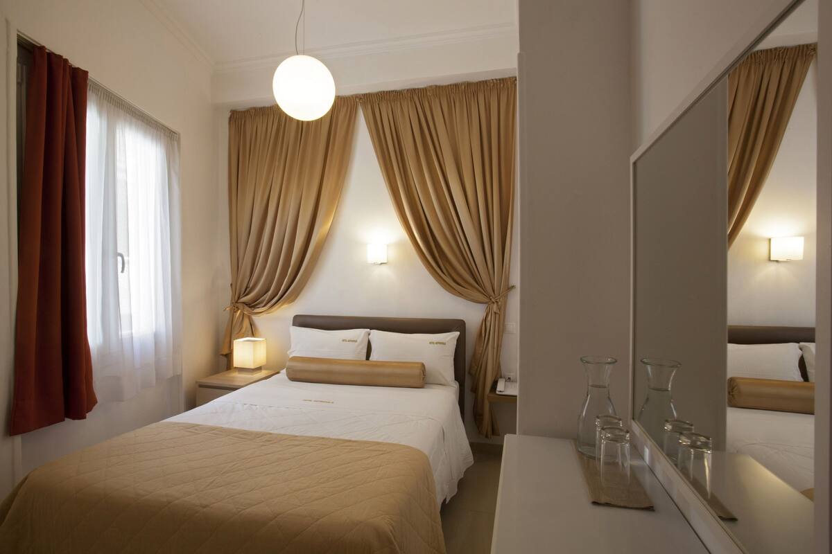 A hotel room with a bed, bedside lamps, a nightstand, a mirror, and curtains.
