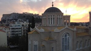 A church with a dome and cross, surrounded by buildings and a hill in the background. - Metropolis Hotel (Athens)