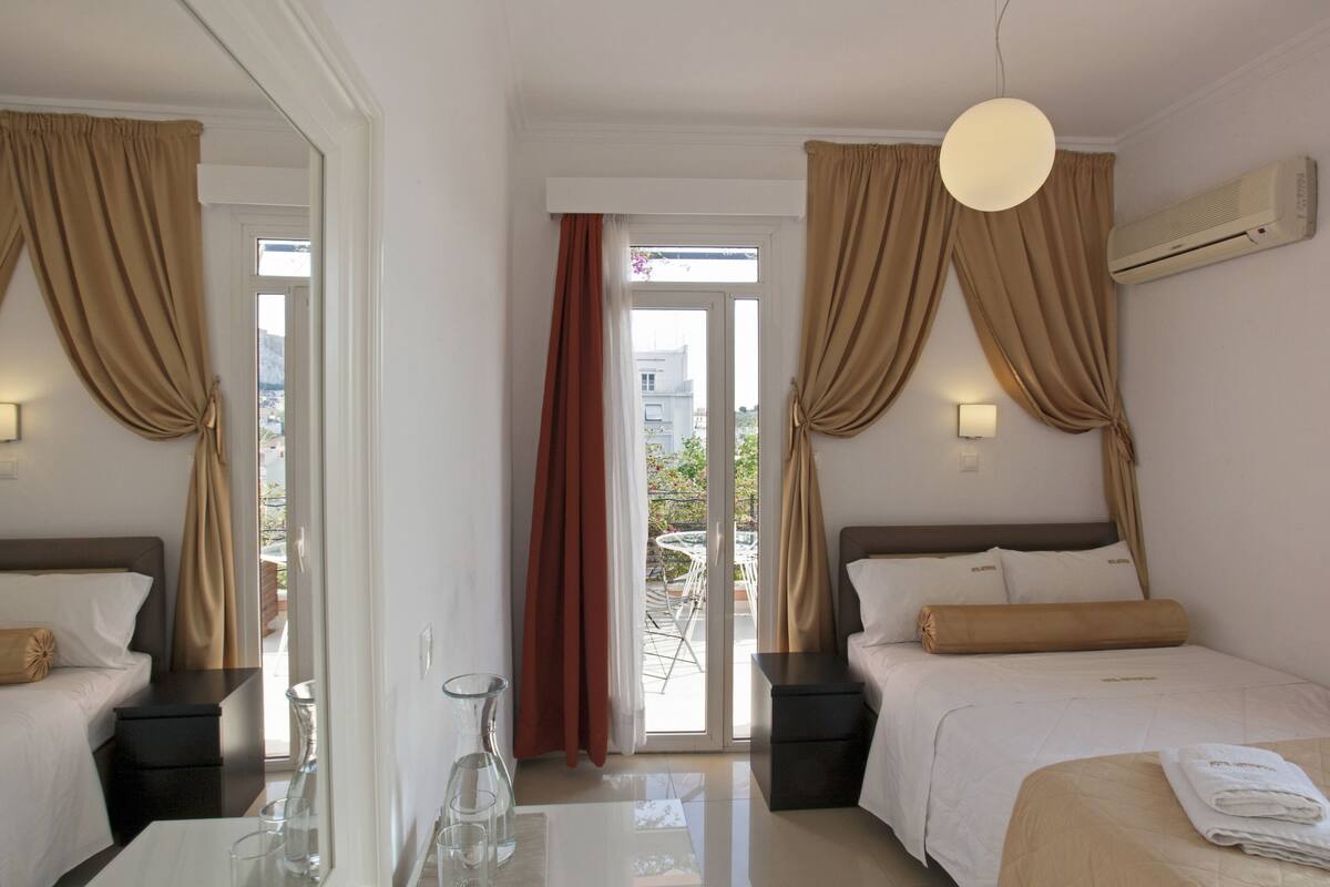 A hotel room with two beds, a glass coffee table, a bedside table with a lamp, and a view of the outside balcony.