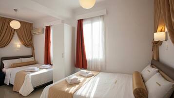 Habitación de hotel con dos camas, un ventanal grande con cortinas, aire acondicionado instalado en la pared y una lámpara en el techo.