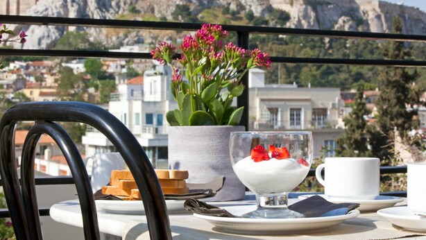 A table with a dessert, a cup, and a flower arrangement, with a view of a historic building in the background. - Metropolis Hotel (Athens)