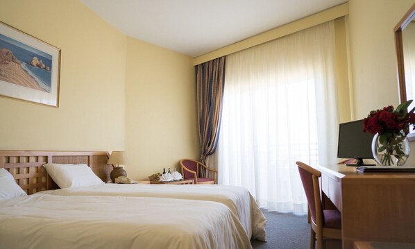 Une chambre d’hôtel avec deux lits, un bureau avec un ordinateur, une chaise, un vase avec des fleurs et un tableau au mur.