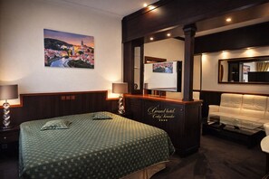 Una habitación de hotel con cama, dos lámparas de noche, un espejo grande, un sofá y una televisión.